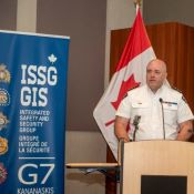 Un policier se tient derrière un podium, devant un drapeau du Canada et des affiches du G7.