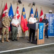 Six hommes en uniforme, provenant chacun d'organismes d'application de la loi et de défense distincts, se tiennent derrière un podium pendant une conférence de presse.