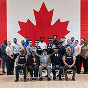 Un groupe de participants et de formateurs posent pour une photo de groupe dans la Salle d'exercice de l'École de la GRC, à la Division Dépôt.