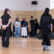 Pendant un exercice d'entraînement policier dans un gymnase, une élève transporte deux sacs d'assistance d'urgence de 45 lb tandis que d'autres observent.