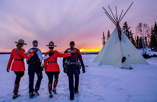 Quatre membres de la GRC marchent dans la neige en direction d'un tipi au coucher du solei