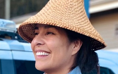 Une femme autochtone portant un chapeau de cèdre sourit en regardant quelque chose hors champ