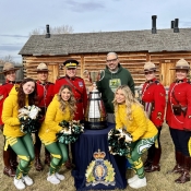 Cinq agents de la GRC en tunique rouge posent avec trois meneuses de claque des Elks d'Edmonton et la Coupe Grey
