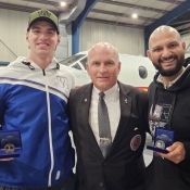 Deux joueurs des Winnipeg Blue Bombers posent avec le gardien de la Coupe Grey devant un avion de la GRC