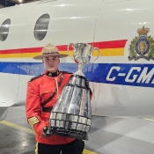 Un officier en tunique rouge pose avec la Coupe Grey devant un avion de la GRC
