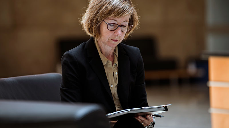 Une femme portant un tailleur noir tient un bloc-notes et un stylo.