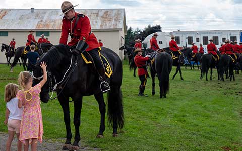 Deux enfants caressent un cheval noir monté par un agent de la GRC.