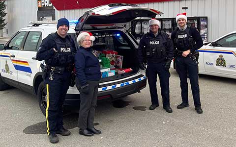 Quatre personnes, dont trois policiers, se tiennent à côté d'un véhicule de police dont le coffre contient des cadeaux.