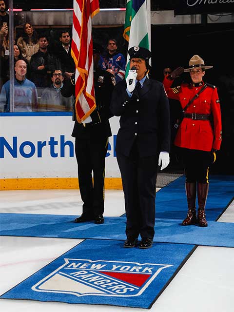Un agent de la GRC, entouré de deux autres personnes, salue sur la glace du Madison Square Garden.