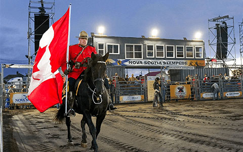 Un agent de la GRC en tunique rouge qui défile à cheval en portant le drapeau canadien.