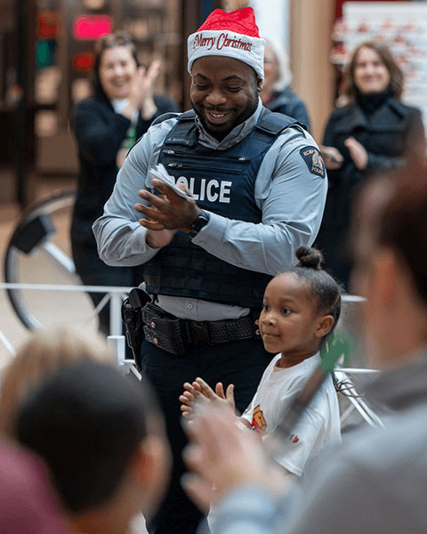 Un agent de la GRC portant un bonnet de Noël se tient à côté d'un enfant tout en applaudissant.