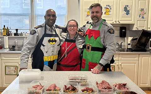 Trois agents de la GRC portant des tabliers dans une cuisine avec les plats qu'ils ont préparés.