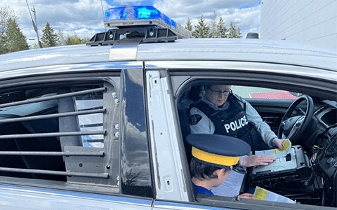 Un agent de la GRC et un enfant non identifiable examinent des documents alors qu'ils sont assis dans une voiture de police.