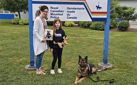 Une femme et un enfant se tiennent debout devant une enseigne de la GRC, avec un chien policier couché à côté d'eux.
