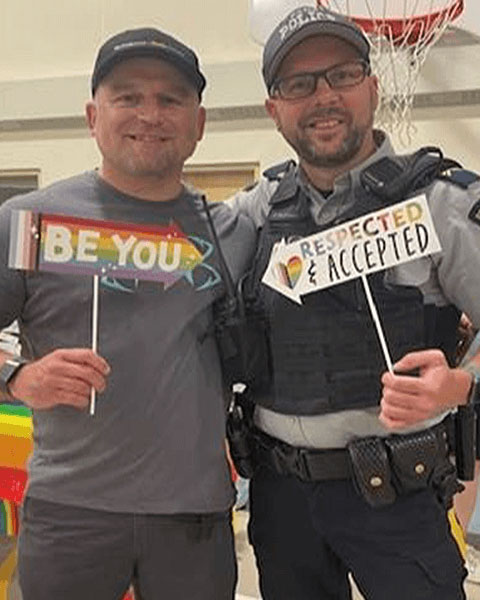 Deux policiers, l'un en civil et l'autre en uniforme, brandissant des pancartes sur lesquelles il est inscrit « Respected and accepted » (Respecté et accepté).