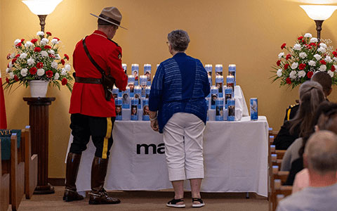 Un agent de la GRC en tunique rouge et un membre du public allument des bougies posées sur une table.
