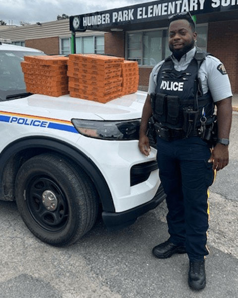 Un agent de la GRC se tient devant son véhicule de police, sur le capot duquel sont posées plusieurs pizzas.