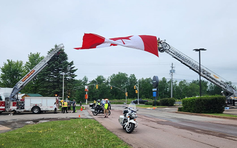 Des motos sont stationnées sous un drapeau canadien hissé par des camions de pompiers.