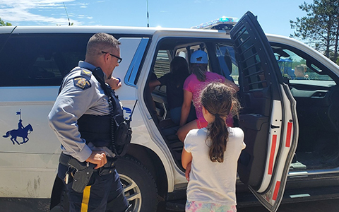 Un agent de la GRC observe des enfants qui examinent son véhicule de police.