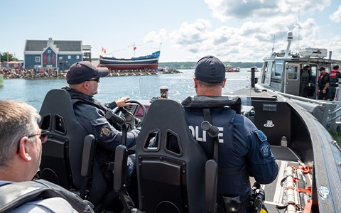 Des agents de la GRC sont assis dans un bateau de patrouille. Le voilier Hector est visible à l’arrière-plan.