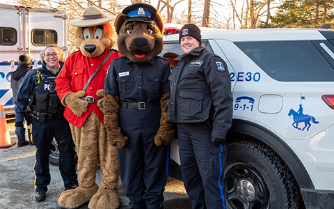 Un agent de la GRC et un agent de la Police régionale d’Halifax posent avec des mascottes devant un véhicule de police.