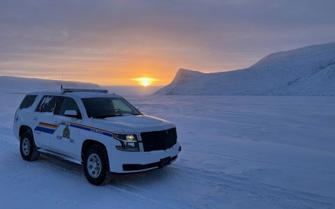 Une voiture de police de la GRC au premier plan d'un paysage enneigé au coucher du soleil.