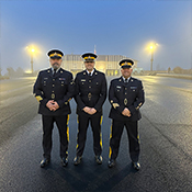 Trois policiers de la GRC debout en uniforme au crépuscule.