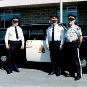 Trois hommes en uniforme de la GRC posent devant un véhicule de patrouille d’époque de la GRC.