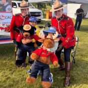 Deux agents en tunique rouge posent souriants avec deux enfants et deux peluches de la GRC.
