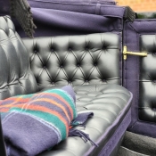 Une couverture bleue, verte et rouge pliée sur le siège en cuir noir à l'intérieur d'une calèche ouverte.