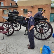 Un homme en combinaison bleue se tient debout à côté d'une calèche. Un autre est assis à l'intérieur en train de polir l'extérieur. Image par Patricia Vasylchuk, GRC.