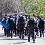 Une troupe de cadets marche dans une rue. Ils portent des sacs à dos et tout leur équipement de police.