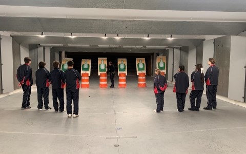 Un groupe d'adolescents en uniforme noir sont alignés à l'intérieur d'un stand de tir