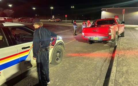 Une camionnette rouge est rangée sur le côté dans un stationnement; un véhicule de patrouille de la GRC est placé derrière, tandis que plusieurs personnes en uniforme se tiennent autour