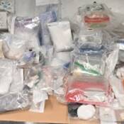 Des dizaines de sacs de preuves transparents remplis de drogues et d’objets divers sur un bureau.