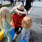 Une gendarme en tunique rouge s’agenouille pendant que deux petites filles jouent avec son chapeau Stetson.
