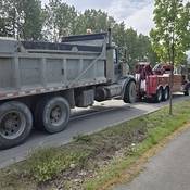 Une dépanneuse rouge se trouvant en bordure de la route tire un gros camion à benne.