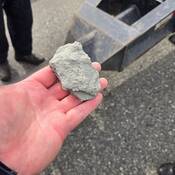 Une pierre dans la main d’un inspecteur de véhicules commerciaux. En arrière-plan, on voit l’essieu d’un véhicule sur une route à Burnaby.