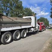 Un gros camion à benne accroché à une dépanneuse rouge sur le bord de la route.