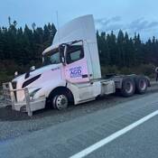 Un camion de transport dans l’accotement en gravier d’une route. Le devant du véhicule est enfoncé dans le gravier et le pneu avant côté conducteur est dégonflé.