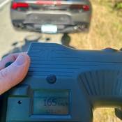 Un lecteur de vitesse au laser indiquant une vitesse de 165 km/h et une Lamborghini grise en arrière-plan.