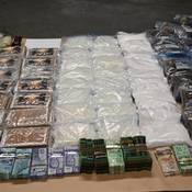 Vue en angle d’une table où se trouvent 97 kg de drogues illicites, dont de la méthamphétamine, de la cocaïne, du fentanyl et du cannabis, ainsi que 70 000 $ en monnaie canadienne et des bijoux.