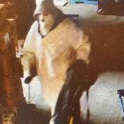 Une image fixe du suspect extraite d’une séquence de vidéosurveillance. Le suspect porte une cagoule, un manteau avec le capuchon relevé et un pantalon blanc, et il transporte un sac de sport noir.