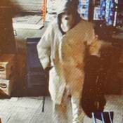 Une image fixe du suspect extraite d’une séquence de vidéosurveillance. Le suspect porte une cagoule, un manteau avec le capuchon relevé et un pantalon blanc, et il transporte un sac de sport noir.