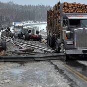Un camion forestier immobilisé sur un pont recouvert de neige et de glace, au milieu de débris. Un semi-remorque blanc fortement endommagé figure en arrière-plan.