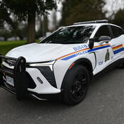 Le nouveau véhicule de patrouille électrique du Détachement de la GRC de Burnaby, un Chevrolet Blazer EV 2024 blanc portant les logos et autocollants de la GRC, stationné à l’extérieur près du détachement.
