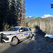 Véhicule de police au bord d’un lac avec des montagnes en arrière-plan.
