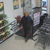 Photo d’un suspect marchant dans l'allée d’entrée et de sortie d’un magasin d’alcool vêtu d'un habit de motoneige, d’une tuque et de lunettes de soleil posées sur le front.