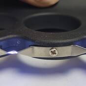 Vue de dessous d'un pistolet paralysant rechargeable en forme de poing américain, composé de plastique et de métal. L'appareil est activé et des arcs électriques sont visibles.