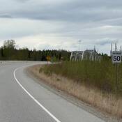 Un tronçon sinueux de la route de l’Alaska près d’Albert Creek dans le secteur d’Upper Liard, avec un panneau indiquant une limite de vitesse maximale de 50 km/h en bordure de la route.